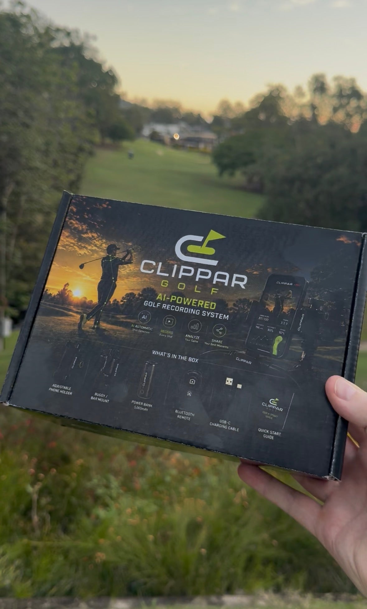Clippar Golf Kit box held up on a golf course at sunset, printed with the contents of the golf swing recording kit